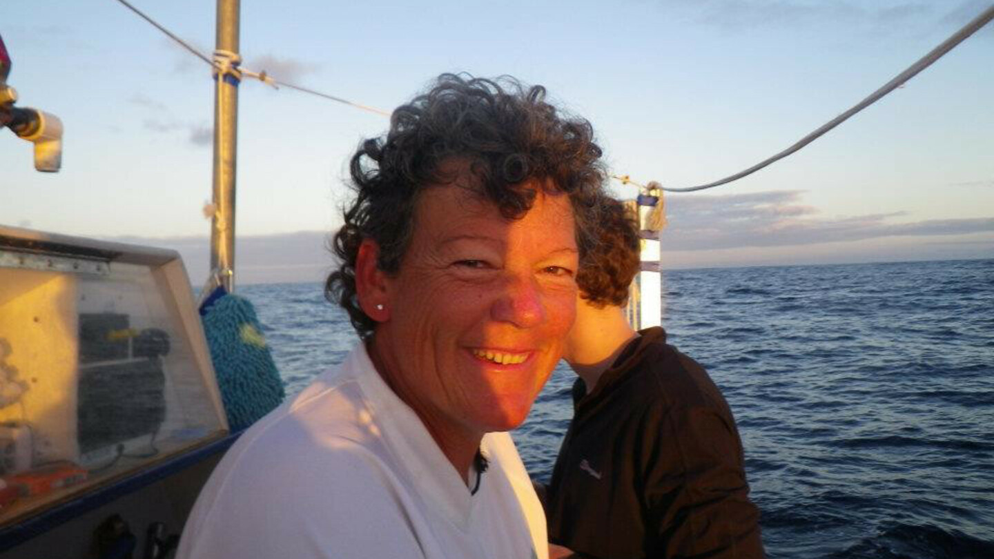 Woman with short curly hair and a white shirt sitting on a boat at sunset, overlooking the open sea.